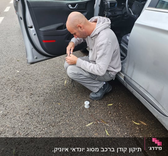 אדם מתקן חוטים ליד דלת רכב פתוחה